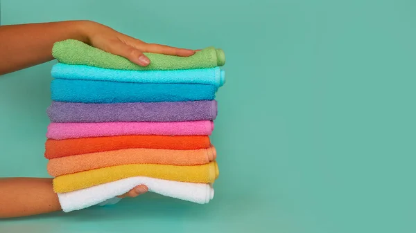 Zbliżenie rąk układających stos świeżych ręczników kąpielowych. stos wielokolorowe czyste ręczniki na niebieskim tle — Zdjęcie stockowe