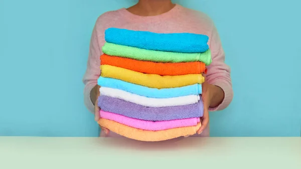 Close-up de mãos colocando pilha de toalhas de banho frescas. rolos multicoloridos de toalhas em uma cesta de vime em um fundo azul — Fotografia de Stock