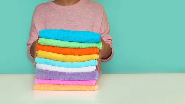 Крупным планом руки кладут стопку свежих полотенец для ванны. разноцветные рулоны полотенец в плетеной корзине на синем фоне — стоковое фото