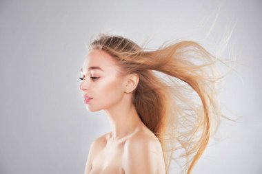 Doğal çıplak makyajlı ve yüzüne dokunan profil mankeni. Spa, cilt bakımı ve sağlık. Yakın plan, gri arkaplan, telif alanı. Rüzgarda dalgalanan saçlar.