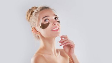 Yeşil arka plan portresi, spa bakımı, kozmetoloji üzerinde gözlerinin altında altın bantlar olan güzel, genç bir kadın. Taze yüz derisi üzerindeki kolajen bantları. Siyah halkalarla savaş