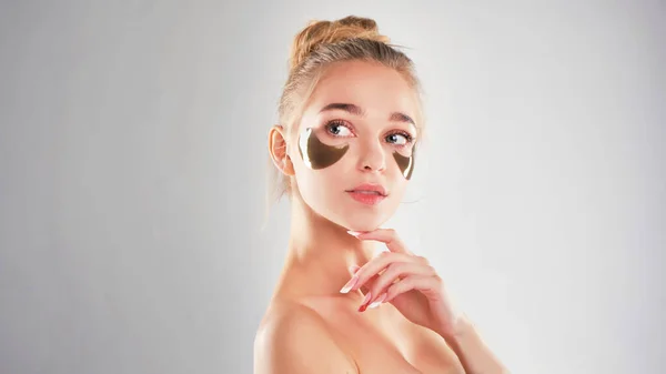 Bela, jovem mulher com manchas de ouro sob os olhos em um retrato de fundo verde, cuidados de spa, cosmetologia. Patches de colágeno na pele facial fresca. luta com círculos escuros — Fotografia de Stock