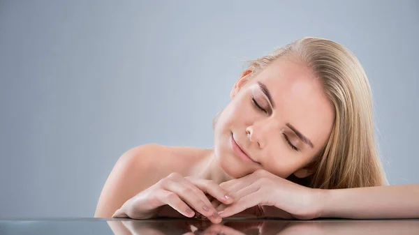 Pretty face of beautiful smiling woman posing at studio on a gray background. hand skin care