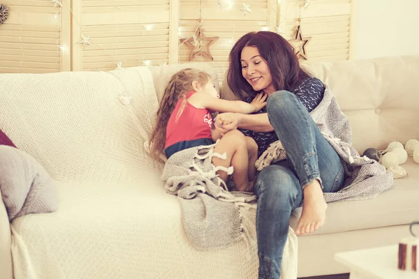 Мама и дочь играют дома на диване. Маленькая девочка щекочет маму. семья веселится вместе — стоковое фото