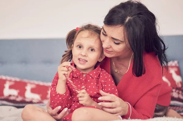 Maman et fille s'amusent ensemble. une femme en pull tricoté rouge chaud serre sa petite fille dans une robe rouge. valeurs familiales — Photo