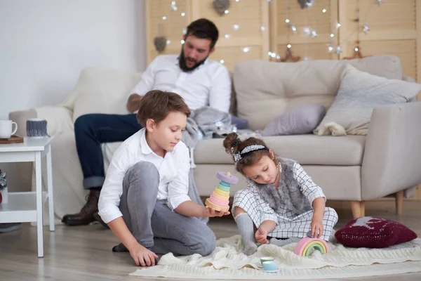 Baba ve çocuklar birlikte eğleniyor, baba kızıyla oğlunu kanepede oynarken izliyor. — Stok fotoğraf