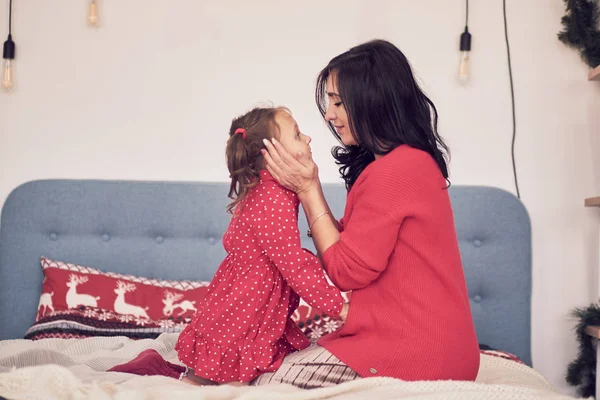 Maman et fille s'amusent ensemble. une femme en pull tricoté rouge chaud serre sa petite fille dans une robe rouge. valeurs familiales — Photo