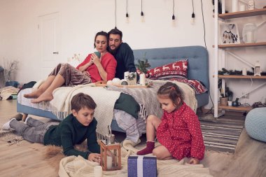 Küçük kız eğleniyor, kardeşler arasında arkadaşlık kuruyor, oturma odasında ailecek vakit geçiriyor. Çocuklar kız ve erkek kardeşler yerde çizim yaparken genç ebeveynler kanepede dinleniyor.