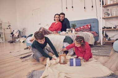 Küçük kız eğleniyor, kardeşler arasında arkadaşlık kuruyor, oturma odasında ailecek vakit geçiriyor. Çocuklar kız ve erkek kardeşler yerde çizim yaparken genç ebeveynler kanepede dinleniyor.