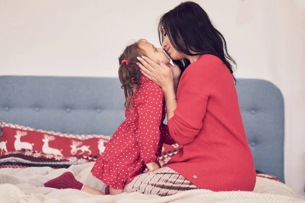 Мама и дочь веселятся вместе. Женщина в тёплом красном трикотажном свитере обнимает свою дочь в красном платье. семейные ценности — стоковое фото