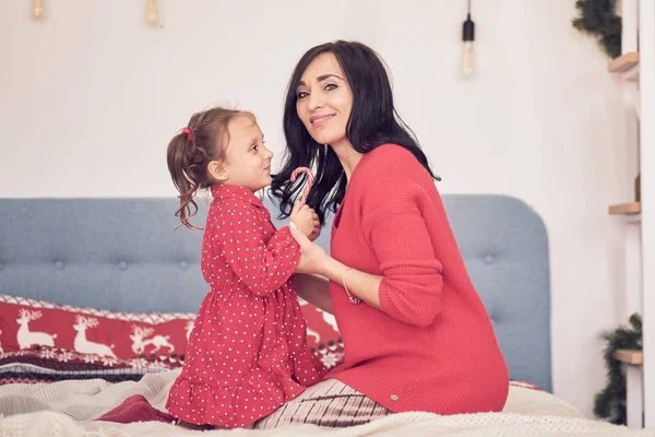 Maman et fille s'amusent ensemble. une femme en pull tricoté rouge chaud serre sa petite fille dans une robe rouge. valeurs familiales — Photo