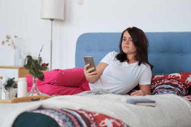 Orta yaşlı bir kadın evde dinleniyor. Yatakta dinlenen kadın telefonunu ve sosyal ağ konseptini kullanır.