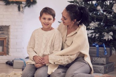 Anne ve oğlu Noel ağacının yanında oynuyorlar. Aile Noel 'i kutluyor. Anne ve oğlu yerde beyaz örgü kazaklarla fotoğraf çektirmek için poz veriyorlar.