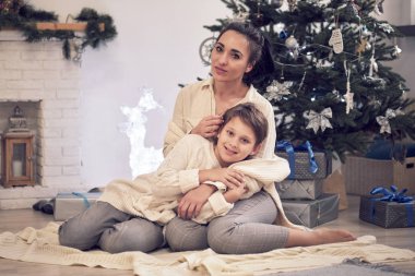 Anne ve oğlu Noel ağacının yanında oynuyorlar. Aile Noel 'i kutluyor. Anne ve oğlu yerde beyaz örgü kazaklarla fotoğraf çektirmek için poz veriyorlar.