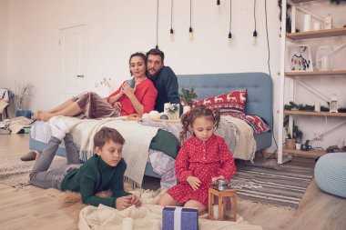 Küçük kız eğleniyor, kardeşler arasında arkadaşlık kuruyor, oturma odasında ailecek vakit geçiriyor. Çocuklar kız ve erkek kardeşler yerde çizim yaparken genç ebeveynler kanepede dinleniyor.