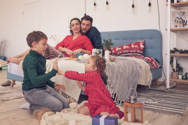 Küçük kız eğleniyor, kardeşler arasında arkadaşlık kuruyor, oturma odasında ailecek vakit geçiriyor. Çocuklar kız ve erkek kardeşler yerde çizim yaparken genç ebeveynler kanepede dinleniyor.