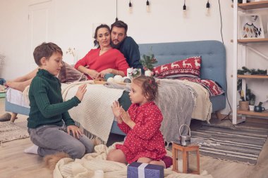 Küçük kız eğleniyor, kardeşler arasında arkadaşlık kuruyor, oturma odasında ailecek vakit geçiriyor. Çocuklar kız ve erkek kardeşler yerde çizim yaparken genç ebeveynler kanepede dinleniyor.