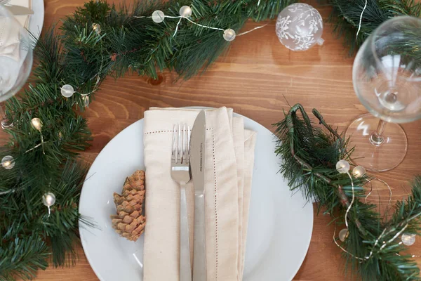Різдвяний стіл з тарілками, посуд, подарункова коробка та прикраси зелених гілок та конусів. на дерев'яному столі — стокове фото