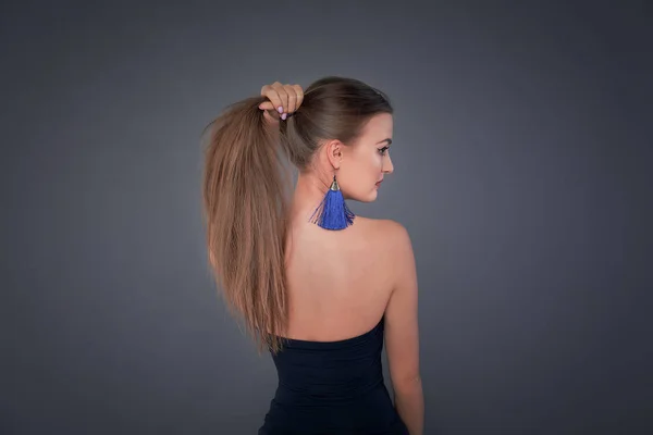 Minimalist photo, Fashionable girl in stylish holding his long hair in the tail, view from the back. long earrings classic blue