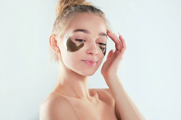Jong mooi zacht vrouw staan naakt kijken camera verzorgen van haar huid met onder oog pleisters. — Stockfoto