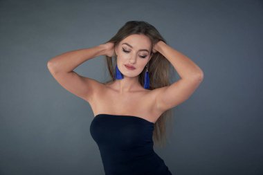 Stüdyoda poz veren uzun kahverengi saçlı güzel bir kadın. Uzun küpeler klasik mavi.