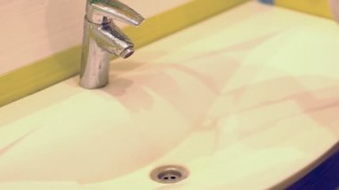 yavaş çekim. Evde banyoda ev işleri yapan kadın, sprey deterjanile lavabo ve musluk temizliği yapıyor. Kırpılmış görünüm