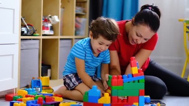 母は息子と一緒にカラフルなプラスチックブロックのおもちゃを演奏し母と息子が一緒に遊ぶための概念. — ストック動画