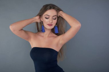 Stüdyoda poz veren uzun kahverengi saçlı güzel bir kadın. Uzun küpeler klasik mavi.