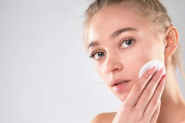 Sağlıklı bir kız pamukla makyajını temizliyor. Sünger gibi arka planda pamuklu ped sorunu olan bir kadın. makyaj sökücü, tonlama,