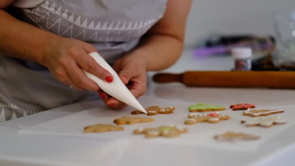 Processo de decoração de biscoitos de Natal. Close up mulher enfeite homens de gengibre caseiros com sorriso triste perto festivo iluminar pinho. Família culinária e tradições conceito . — Vídeo de Stock