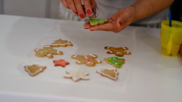 Διαδικασία διακόσμησης χριστουγεννιάτικα μπισκότα. Κοντινό πλάνο Γυναίκα γαρνίρισμα σπιτικό μελόψωμο ανδρών με θλιβερό χαμόγελο κοντά σε εορταστική φωτίζει πεύκο. Οικογενειακή μαγειρική και παραδόσεις έννοια. — Αρχείο Βίντεο