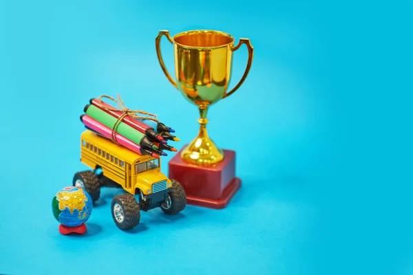 Trophée des lauréats d'or et bus scolaire jaune et stylos feutre sur le toit, concept de retour à l'école, fond jaune, espace de copie. l'éducation. isolé sur fond bleu — Photo