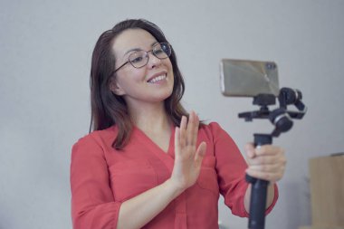 Çekici Asyalı kadın blogcu ya da video blogcu kameraya bakıyor ve teknoloji ile video çekiminde konuşuyor. Sosyal medya insanları veya içerik üreticisi kavramını evde rahat bir şekilde etkiledi.