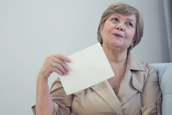 Aşırı ısınmış yaşlı kadın kanepede oturmuş serinlemek için yelpaze sallıyor, 60 yaşında kadın kendini kötü hissediyor, yaş hormonu değişimleri, klimasız daireler, yaz mevsimi rahatsızlık konsepti.