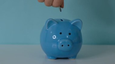 Piggy Bank iş konsepti. Bir el, mavi arka plandaki kumbaraya para koyuyor. Para biriktirmek gelecek için bir yatırımdır. Banka yatırımı.