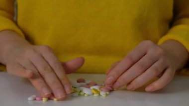 Kadın eli beyaz masadaki farklı hapları sınıflandırıyor. İlaç şişesinden alınan hapları, vitaminleri veya hapları gösteriyor.