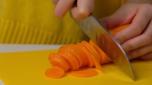 Жінка розрізає моркву на столі, крупним планом. Руки розрізають моркву на обробній дошці. Молода жінка ріже овочі на кухні. Повільний рух . — стокове відео