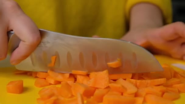 Жінка розрізає моркву на столі, крупним планом. Руки розрізають моркву на обробній дошці. Молода жінка ріже овочі на кухні. Повільний рух . — стокове відео