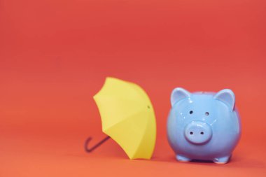 Kırmızı arka planda sarı şemsiyeli domuzcuk kumbarası. tasarruf birikimi.