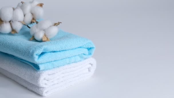Toallas limpias blancas y azules y una rama de algodón sobre un fondo blanco. Primer plano: cámara lenta . — Vídeo de stock