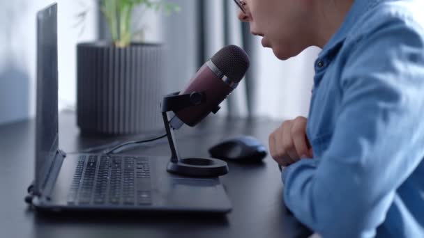 Retrato de una joven blogger conduciendo una transmisión en vivo, habla en un micrafón. mujer lleva podcast en casa delante de la computadora portátil — Vídeo de stock