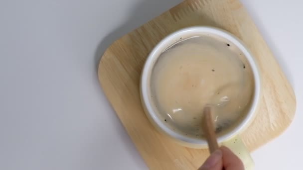 Vista dall'alto di Persona mano sterzo caffè in una tazza con cucchiaio. Mattina di colazione di una tazza di caffè nero caldo su sfondo bianco. Primo piano rallentatore . — Video Stock