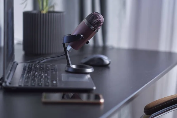 Laptop, smartphone, micrófono en una mesa negra. concepto de lugar de trabajo de un blogger que está a punto de liderar un podcast . — Foto de Stock