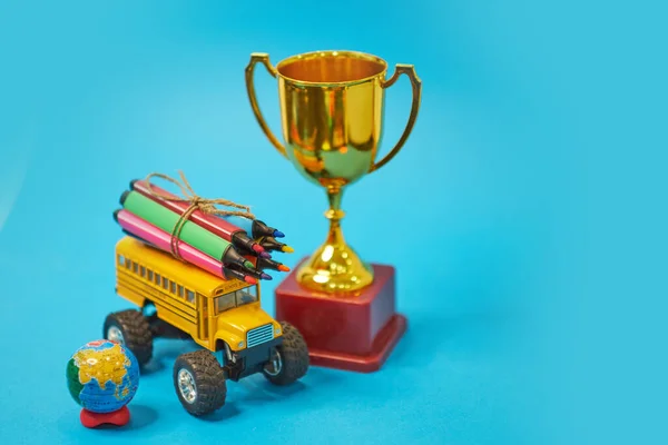 Trophée des lauréats d'or et bus scolaire jaune et stylos feutre sur le toit, concept de retour à l'école, fond jaune, espace de copie. l'éducation. isolé sur fond bleu — Photo