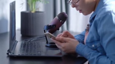 Canlı yayın yapan genç bir kadın blogcunun portresi bir mikronla konuşuyor. Kadın dizüstü bilgisayarın önünde podcast 'i yönetiyor.