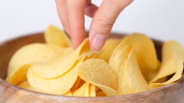 Aardappel chips kom op witte achtergrond. Close-up hand van het vrouwtje dat chips uit de kom neemt. Closeup Slow motion. — Stockvideo