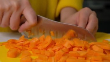 Masada havuç kesen kadın, yakın plan. Kesme tahtasının üzerinde havuç kesen eller. Mutfakta sebze doğrayan genç bir kadın. Yavaş çekim.