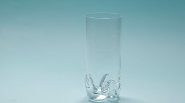 Stüdyoda çekilen su mavi arka planda şeffaf cama dökülüyor. Slow Motion videosu. Üst görünümü kapat