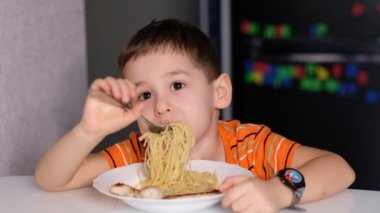 child playing with pasta at dining table. messy face eating. sauce and kid. boy eats pasta noodles sitting in nursery cafe. Happy child eating healthy organic and vegan food in restaurant.