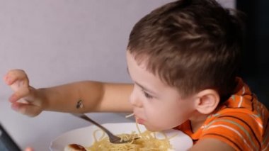 child playing with pasta at dining table. messy face eating. sauce and kid. boy eats pasta noodles sitting in nursery cafe. Happy child eating healthy organic and vegan food in restaurant.
